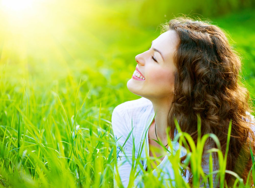 Zufriedene glückliche junge Frau genießt Sonnenstrahlen auf einer Wiese
