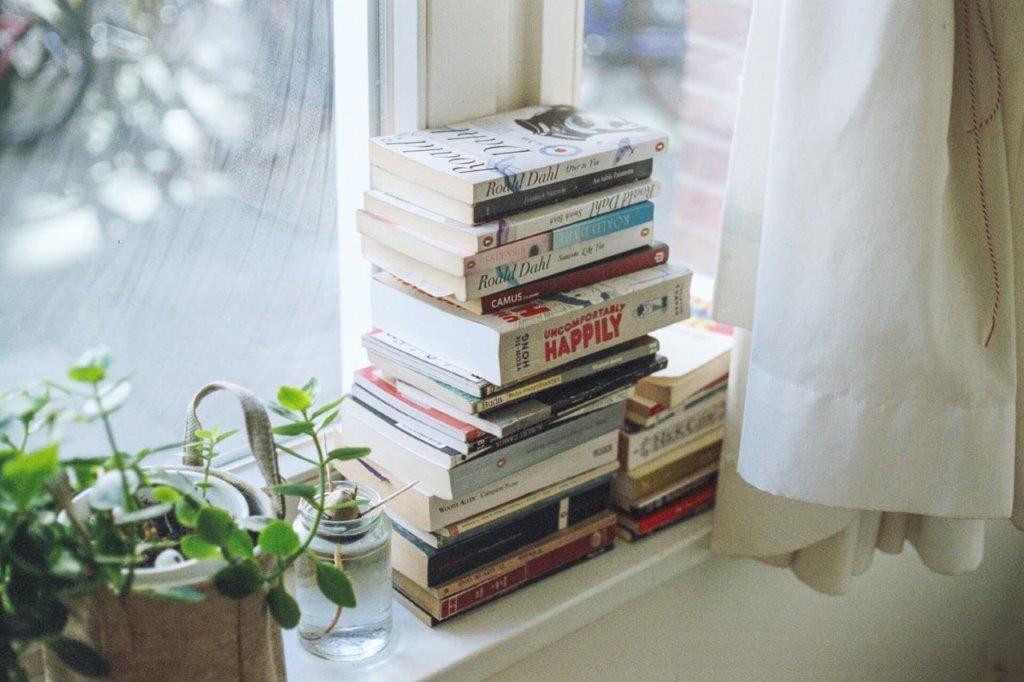 Ein Stapel Bücher auf einem Fensterbrett neben Grünpflanzen
