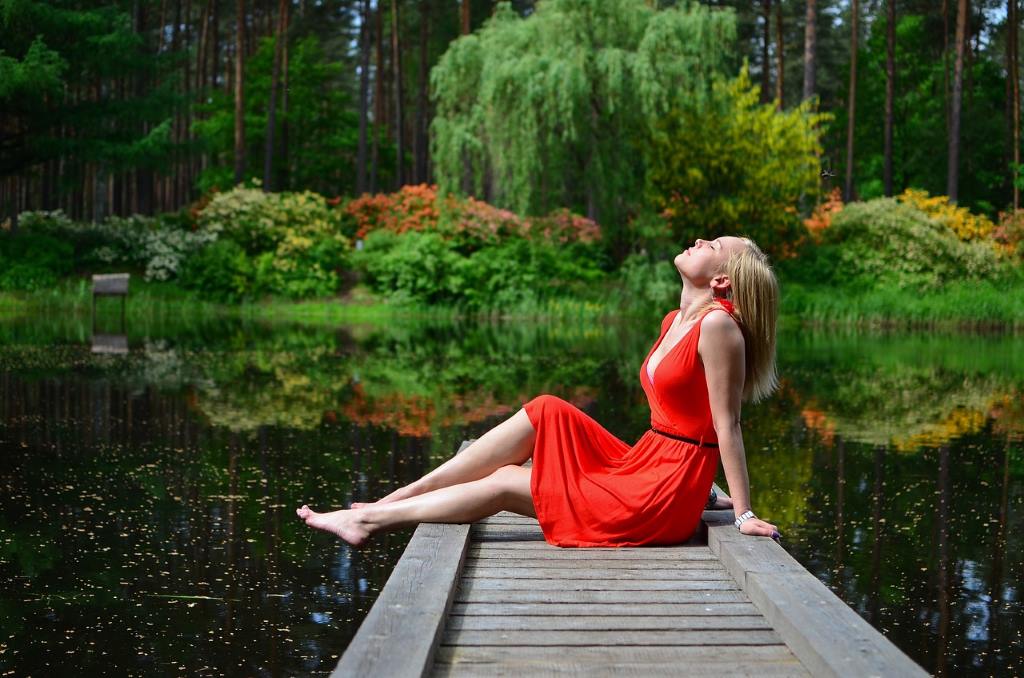 Mein August 2023: Frau mit rotem Kleid sitzt auf einem Holzsteg am See